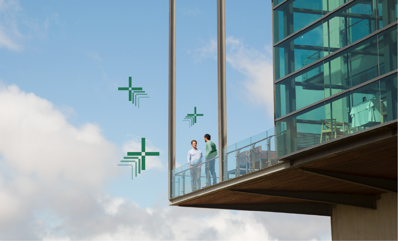 Two men in a high-rise building with the sky with clouds behind them, having a discussion implying collaboration