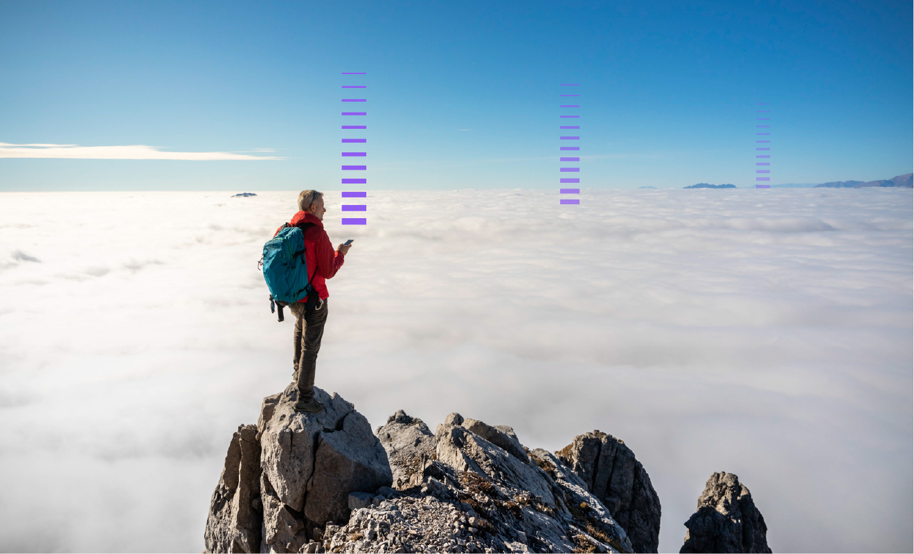 A male hiker with a blue backpack, red jacket and cell phone at the top of a mountain admiring the expanse of clouds in front of him